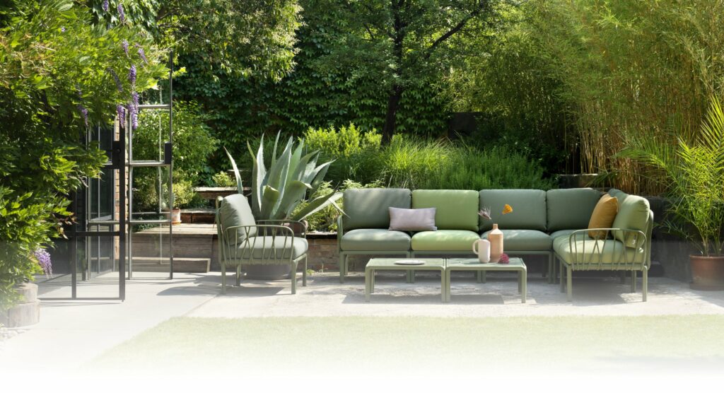 A green nardi komodo modular outdoor lounge in a leafy backyard with a coffee table and arm chair